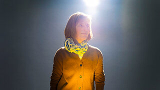 Eine Frau steht in einem sanften Lichtstrahl, der eine ruhige und nachdenkliche Atmosphäre schafft, symbolisch für das Thema Nahtoderfahrung.