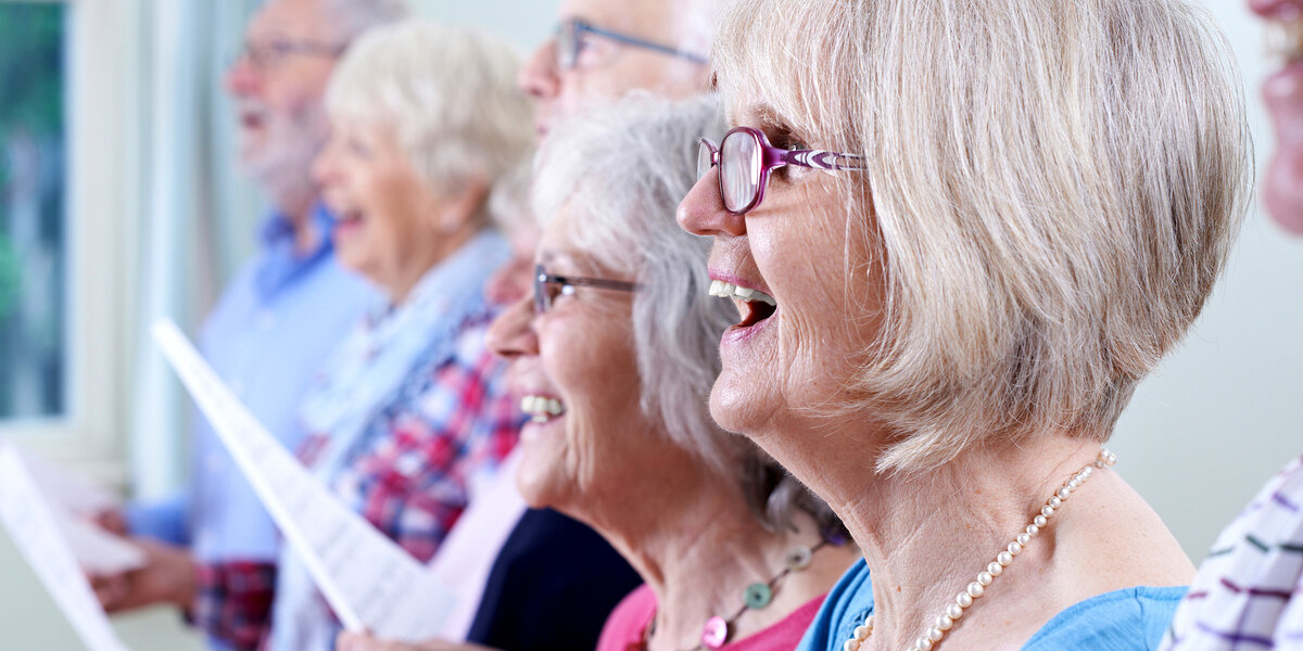 Mehrere Seniorinnen und Senioren sind von der Seite zu sehen und singen im Chor.