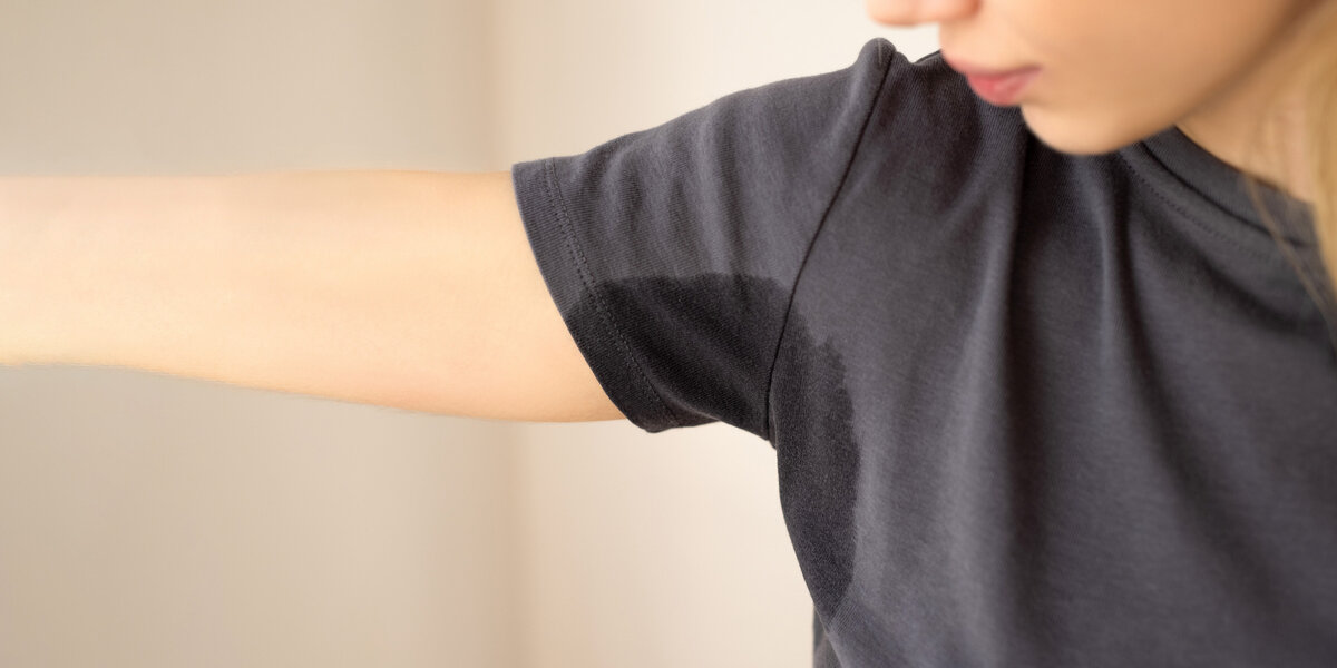 Frau mit Schwitzflecken auf dem Shirt unter der Achsel