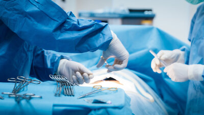 Ein Chirurgenteam arbeitet während einer Operation, umgeben von chirurgischen Instrumenten und blauem Abdecktuch.